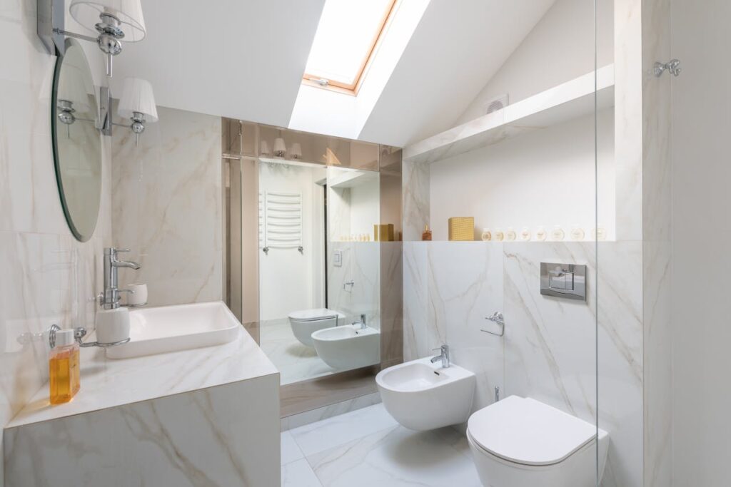 Interior of light restroom with sink on marble cupboard against white bidets and mirror on wall and window on ceiling